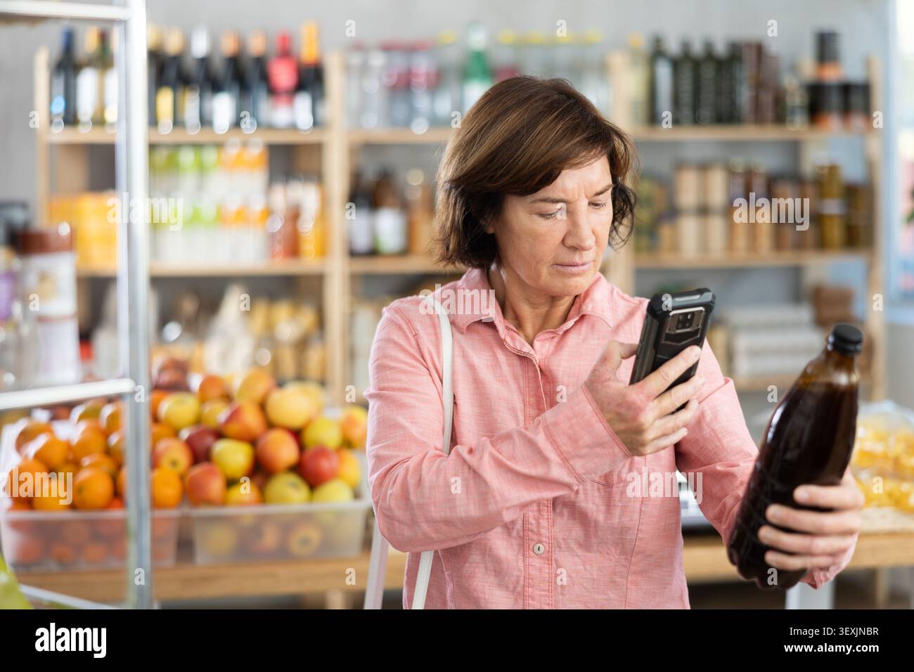 L'acquirente donna esegue la scansione del codice QR sull'etichetta della birra nel negozio di alimentari Foto Stock