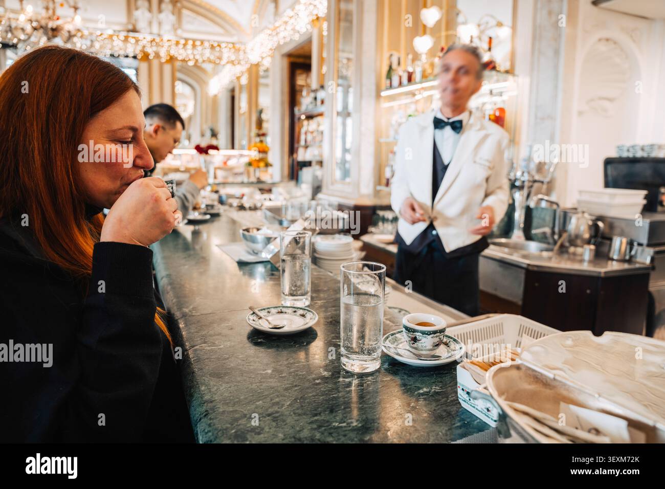 Napoli, Italia, 31 gennaio 2025: Una donna beve un espresso in un bar di marmo come cameriere al servizio dei clienti. Foto Stock