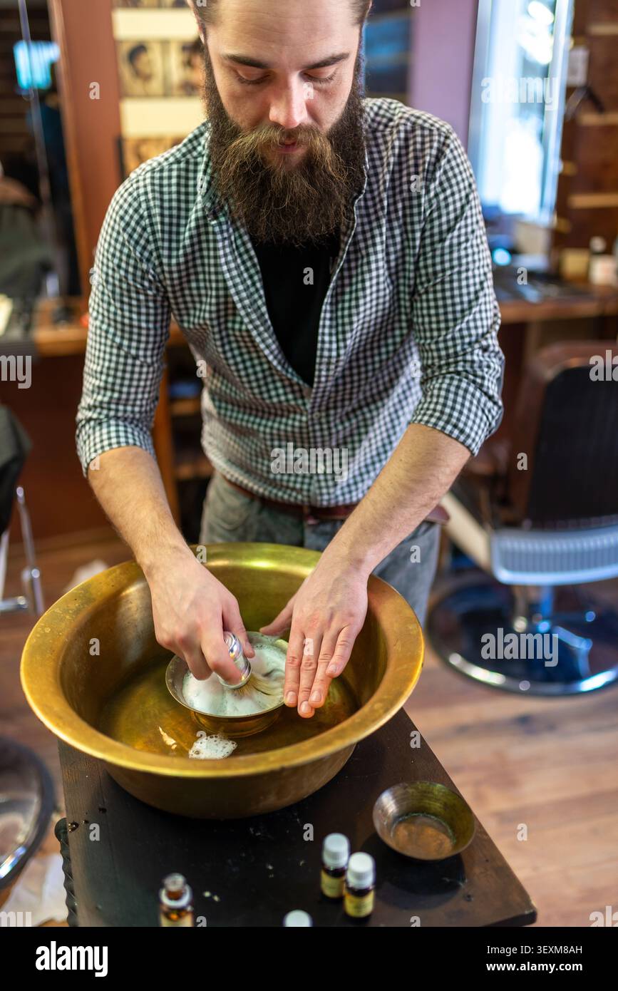 Barbiere prepara una schiuma da barba ricca in un tradizionale recipiente in ottone Foto Stock