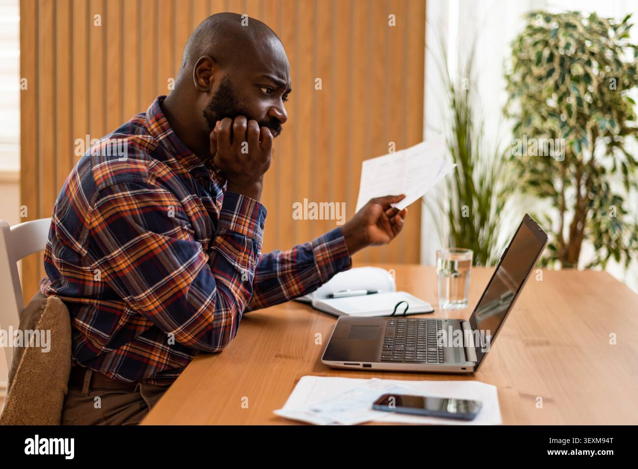 Ansioso uomo nero che esamina i documenti finanziari e calcola le spese. Foto Stock