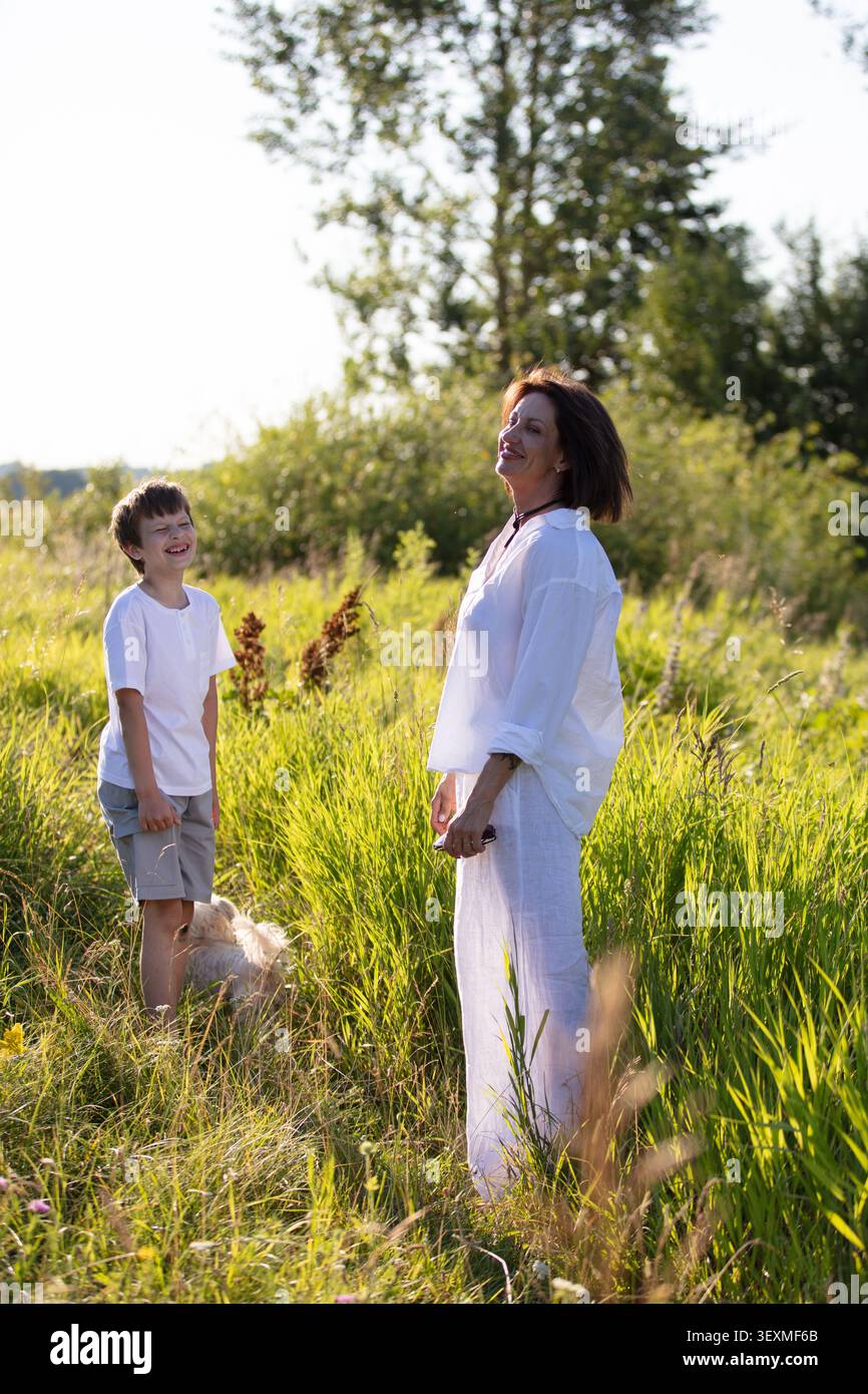 Una donna e un bambino condividono un momento felice in un vivace campo verde. Il sole splende caldamente mentre interagiscono giocherellamente, circondati da erba e gent lussureggianti Foto Stock