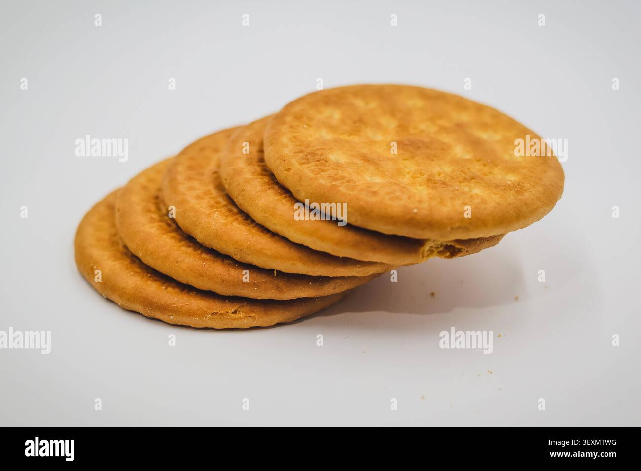 Pila di biscotti rotondi marrone dorati su uno sfondo bianco, pila inclinata di biscotti rotondi croccanti Foto Stock