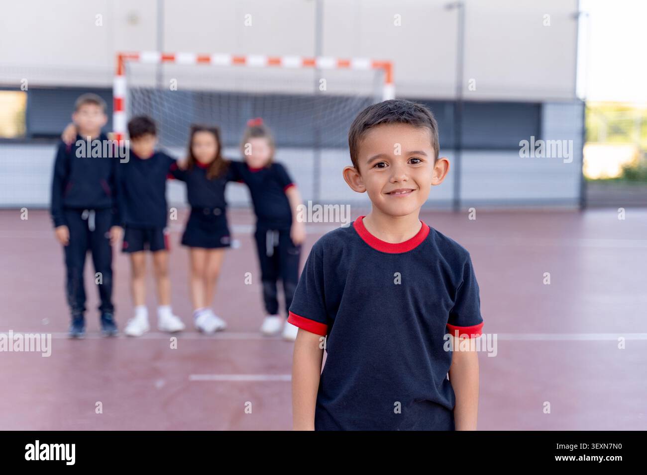 Studente sorridente alla macchina fotografica durante la lezione di educazione fisica. Compagni di classe in piedi con un obiettivo e campo in background Foto Stock