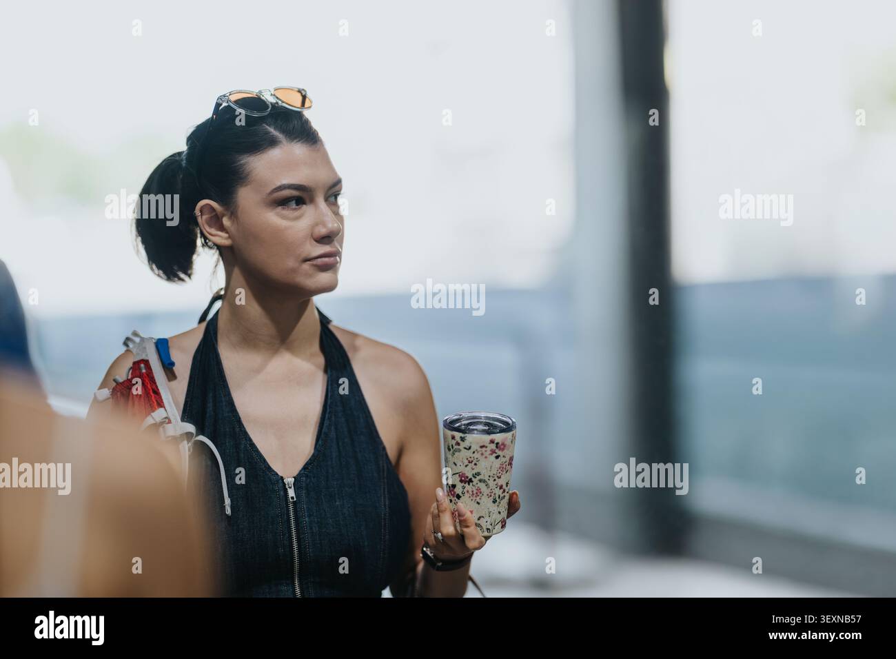 Giovane donna turistica che tiene in mano una tazza da viaggio mentre una troupe di telecamere filma sullo sfondo Foto Stock