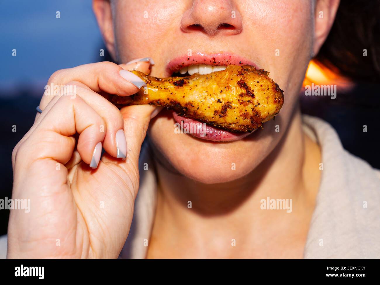 Primo piano di una donna che mangia una deliziosa ala di pollo Foto Stock