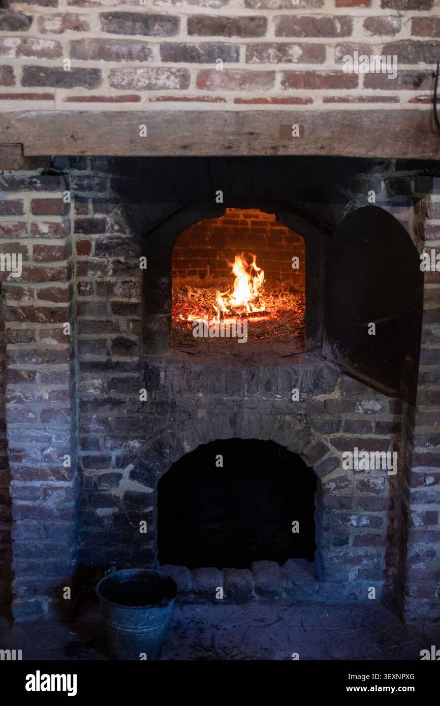 Forno a legna in mattoni rustici con fuoco acceso e utensili da forno tradizionali nella cucina storica Foto Stock