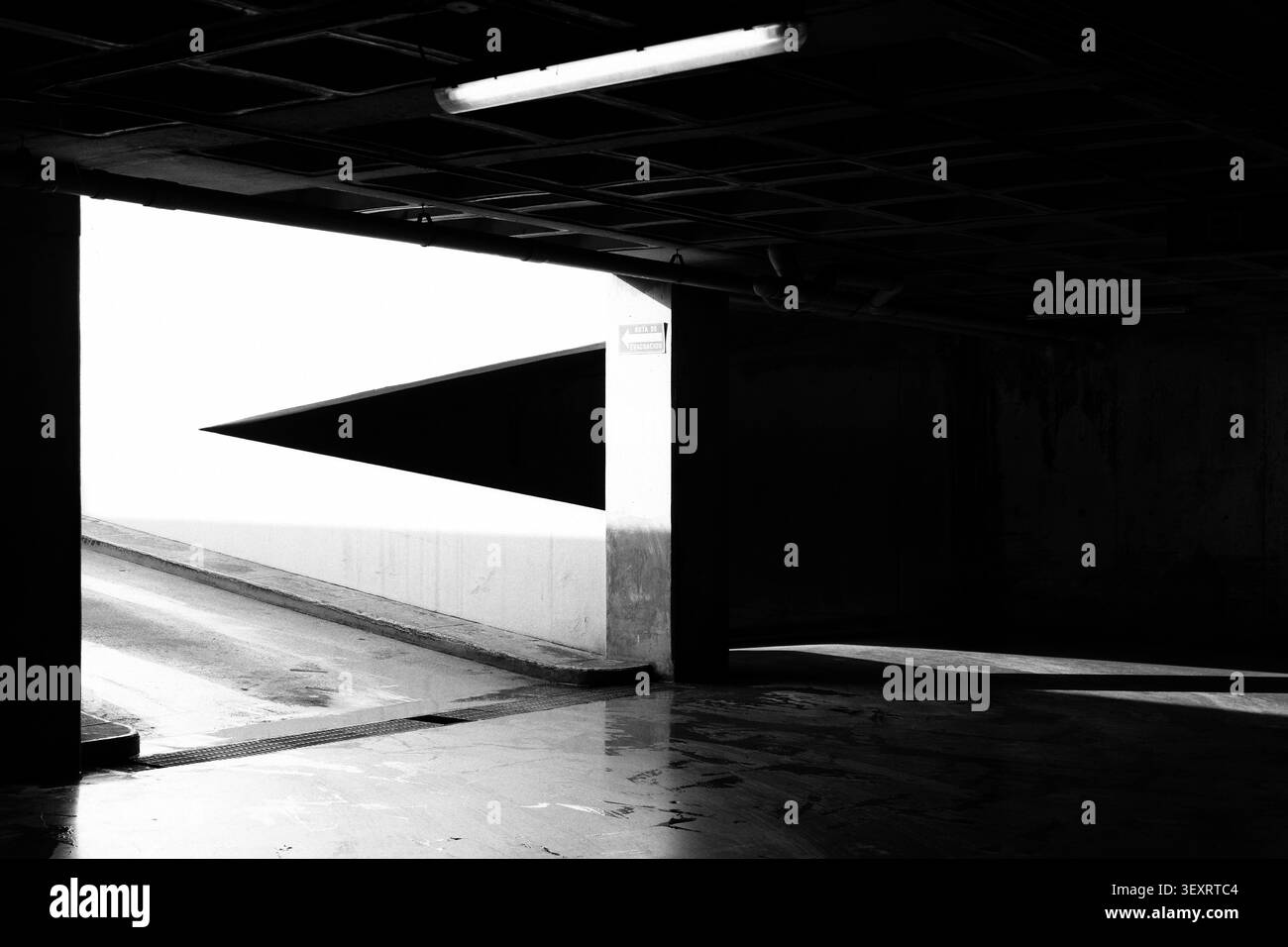 Bianco e nero interni suggestivi del garage sotterraneo con forte contrasto, luce di uscita luminosa e ombre geometriche Foto Stock