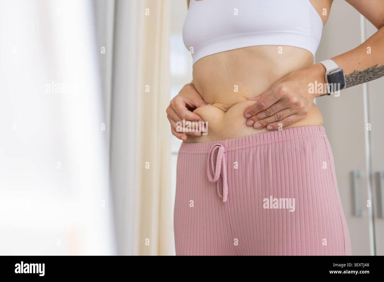 Donna che pizzica la pelle del pancino e le maniglie d'amore, controlla l'eccesso di grasso, lavora sulla trasformazione del corpo, il viaggio di perdita di peso, gli obiettivi di fitness e Foto Stock