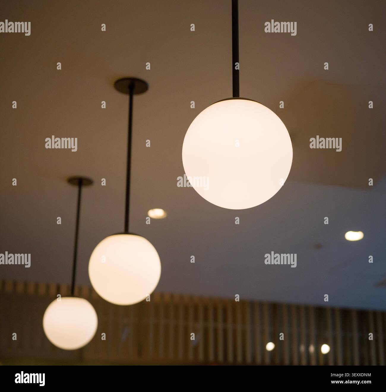 Interni dal design minimalista con una fila di luci a sospensione a globo smerigliate che pendono dal soffitto. Foto Stock