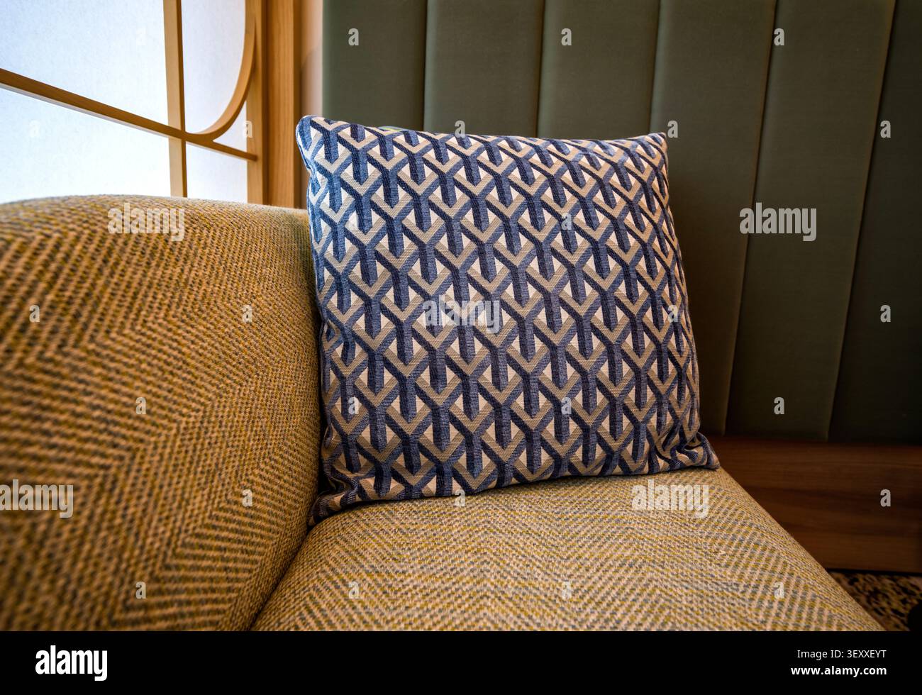 Un cuscino a gettoni blu e grigio a motivi geometrici su un divano in chevron testurizzato in un moderno interno in stile giapponese. Foto Stock