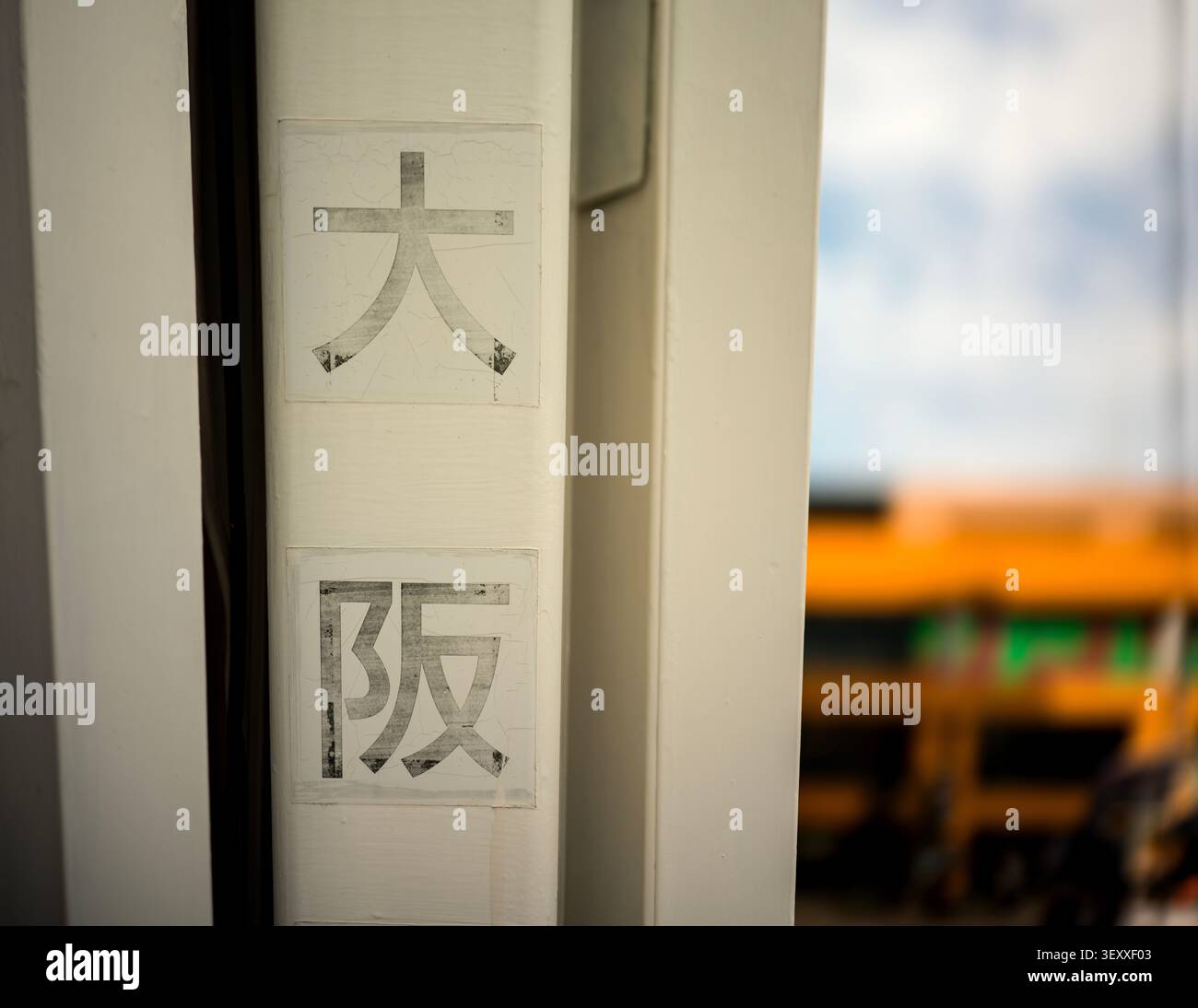 Primo piano di personaggi Kanji intemprati che leggono "Osaka" su una struttura bianca, con uno sfondo urbano sfocato. Foto Stock