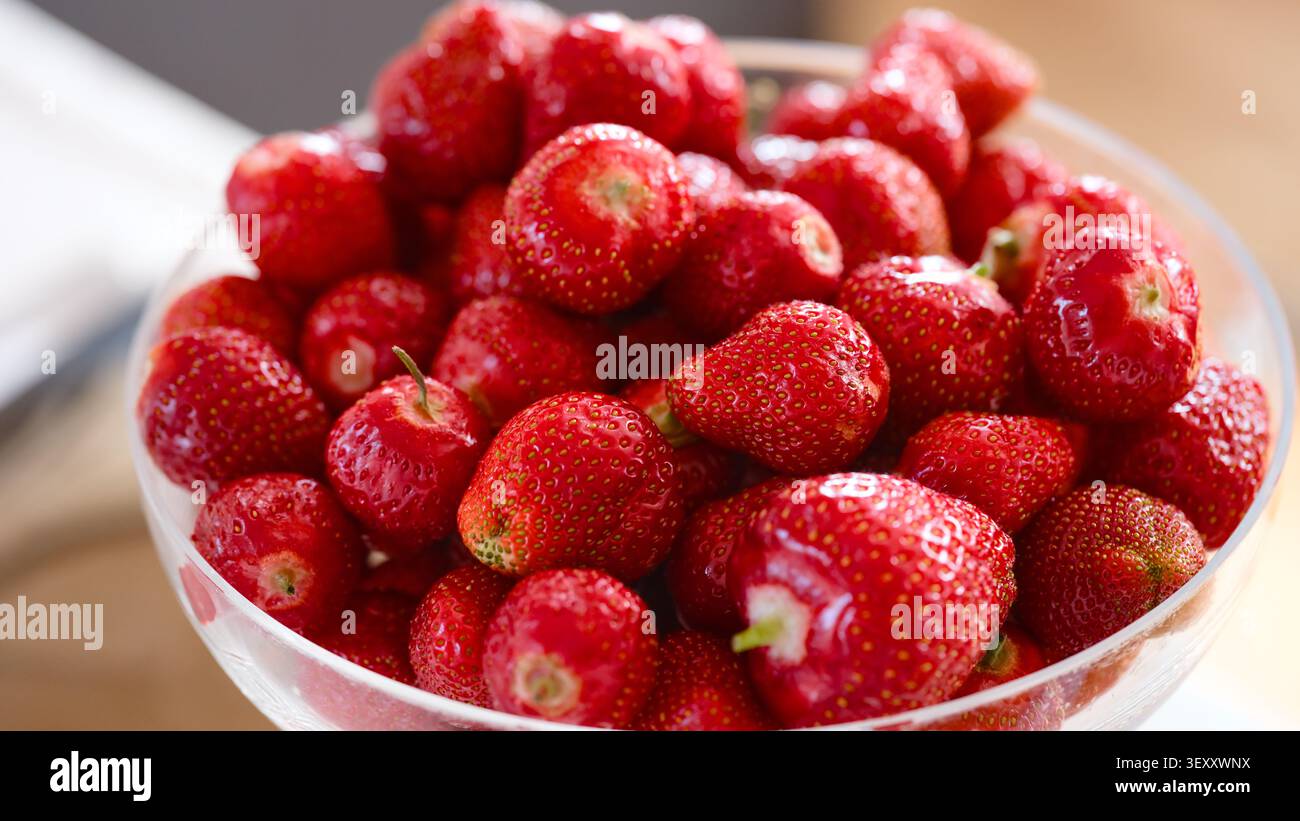 Uno shot ravvicinato di una ciotola di vetro piena di fragole rosse mature fresche. Foto Stock
