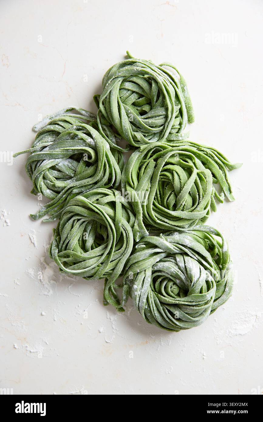 La pasta verde fatta in casa nidifica con farina su una superficie bianca, preparazione tradizionale del cibo italiano Foto Stock