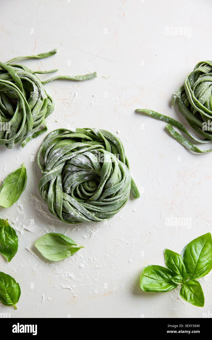 Tagliatelle di spinaci verdi preparate con basilico fresco su una superficie bianca Foto Stock