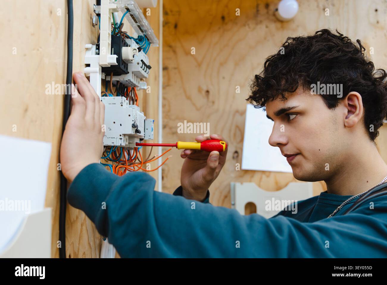 Studente maschile specializzato che utilizza un cacciavite su un complesso gruppo di interruttori per circuito stampato di formazione in officina a scho Foto Stock