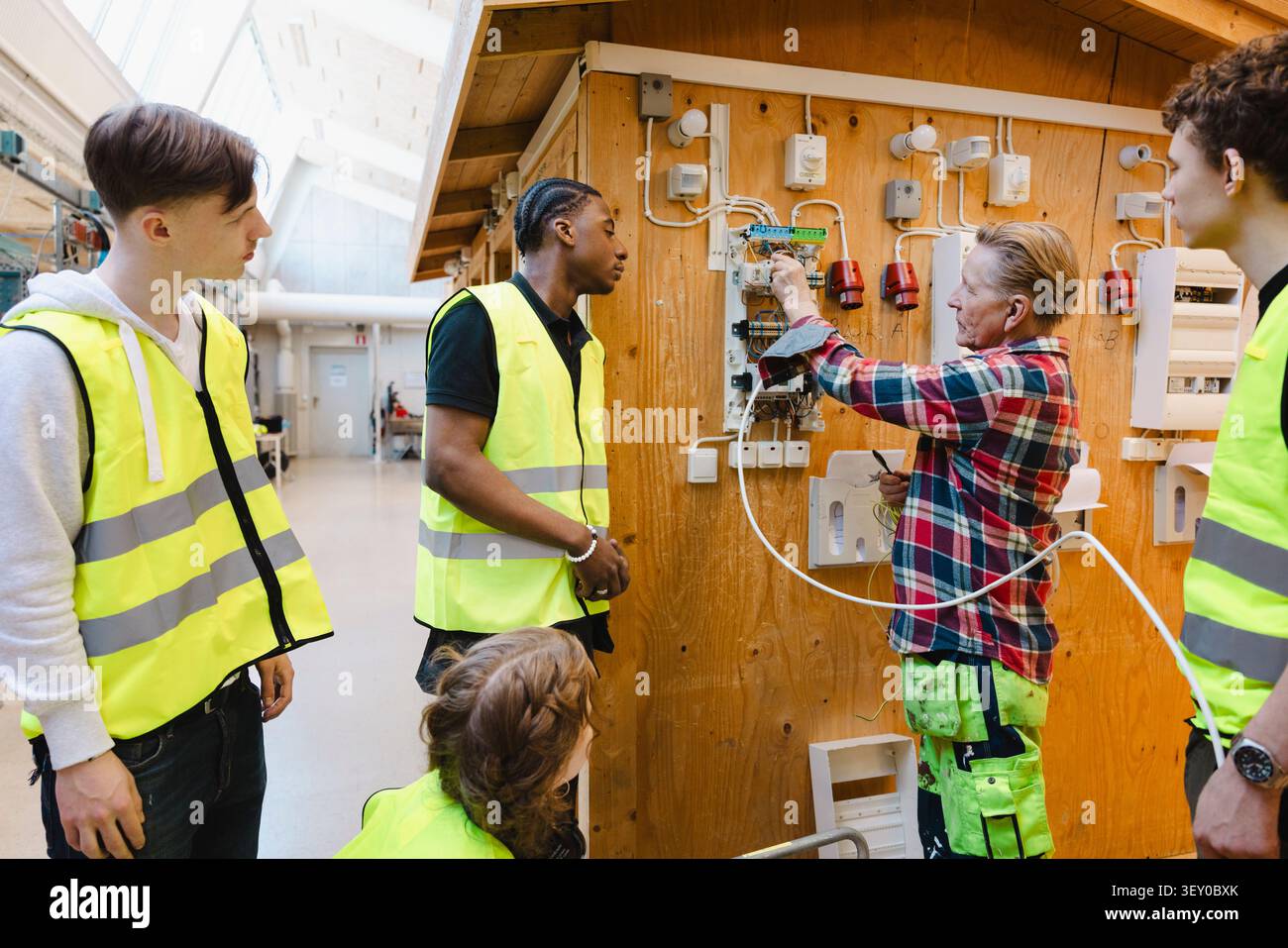 Ingegnere maschio senior che insegna agli studenti il cablaggio del circuito elettrico in una sessione di formazione presso un'officina professionale Foto Stock
