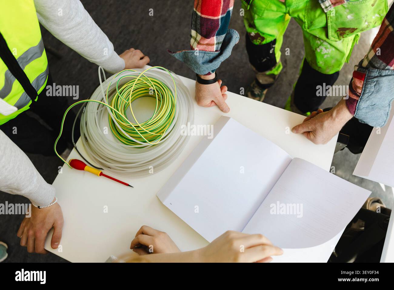 Vista ad alto angolo di studenti e insegnanti che esaminano il manuale tecnico aperto con schemi elettrici nel libro in aula Foto Stock