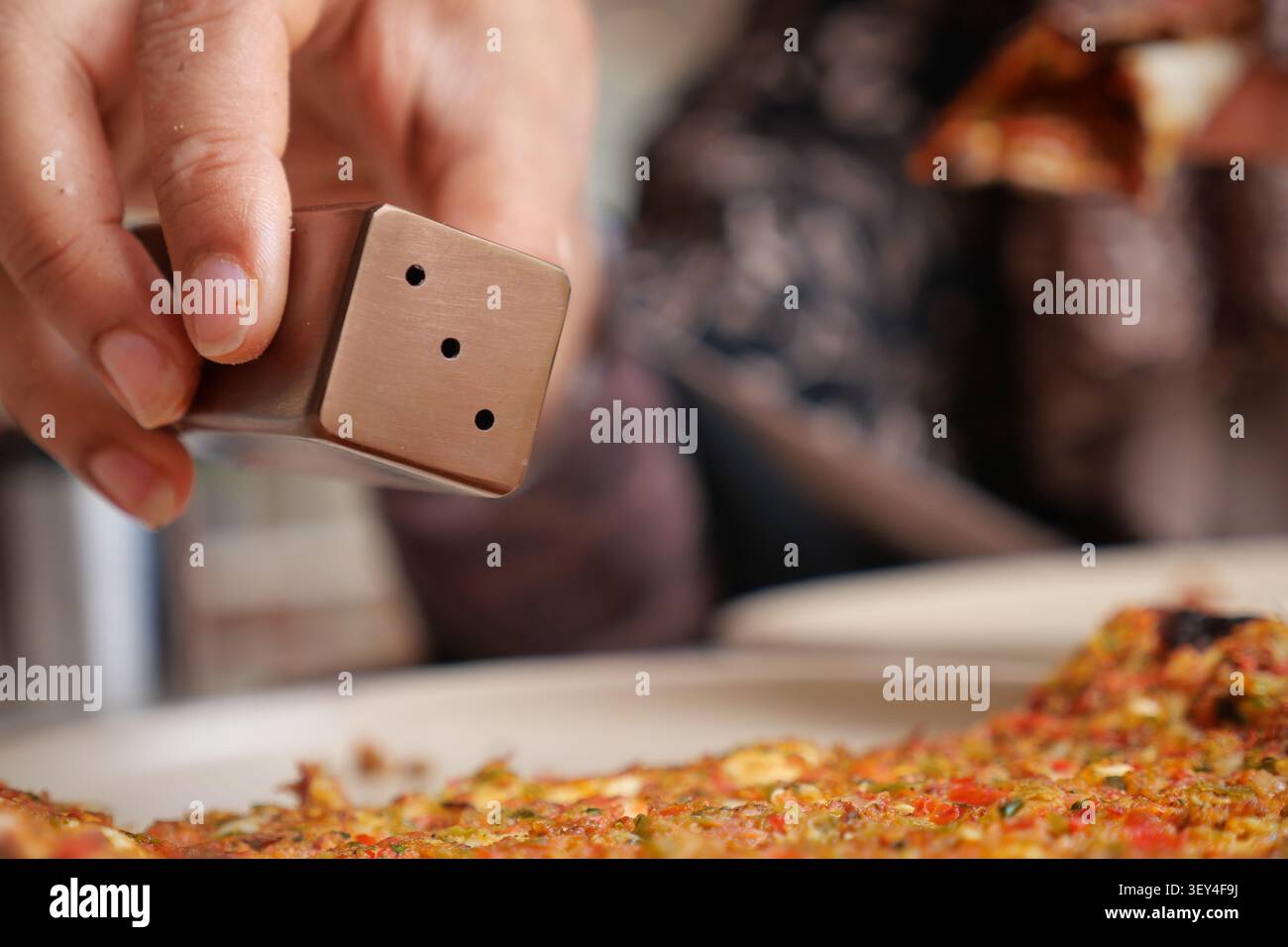 La persona aggiunge sale a una pizza durante l'ora del pasto Foto Stock