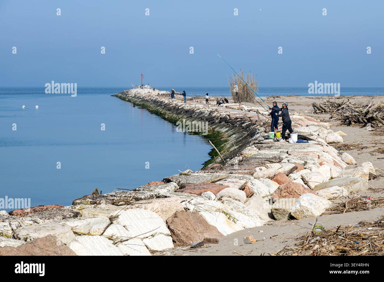 Chioggia, Italia - 8 marzo 2026: Pescatori che gettano le linee sul molo roccioso alla foce del Brenta-Bacchiglione sul Mare Adriatico, Veneto Foto Stock
