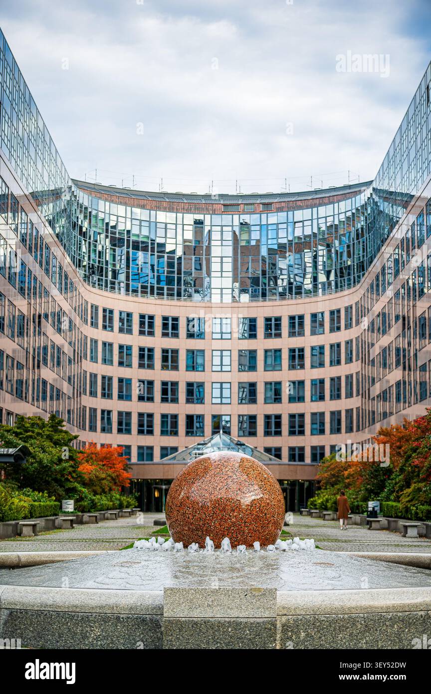 Cortile moderno dell'ufficio a Berlino, Germania, con una fontana a sfera in granito lucido in primo piano, incorniciata da un ufficio in vetro e pietra curvo Foto Stock