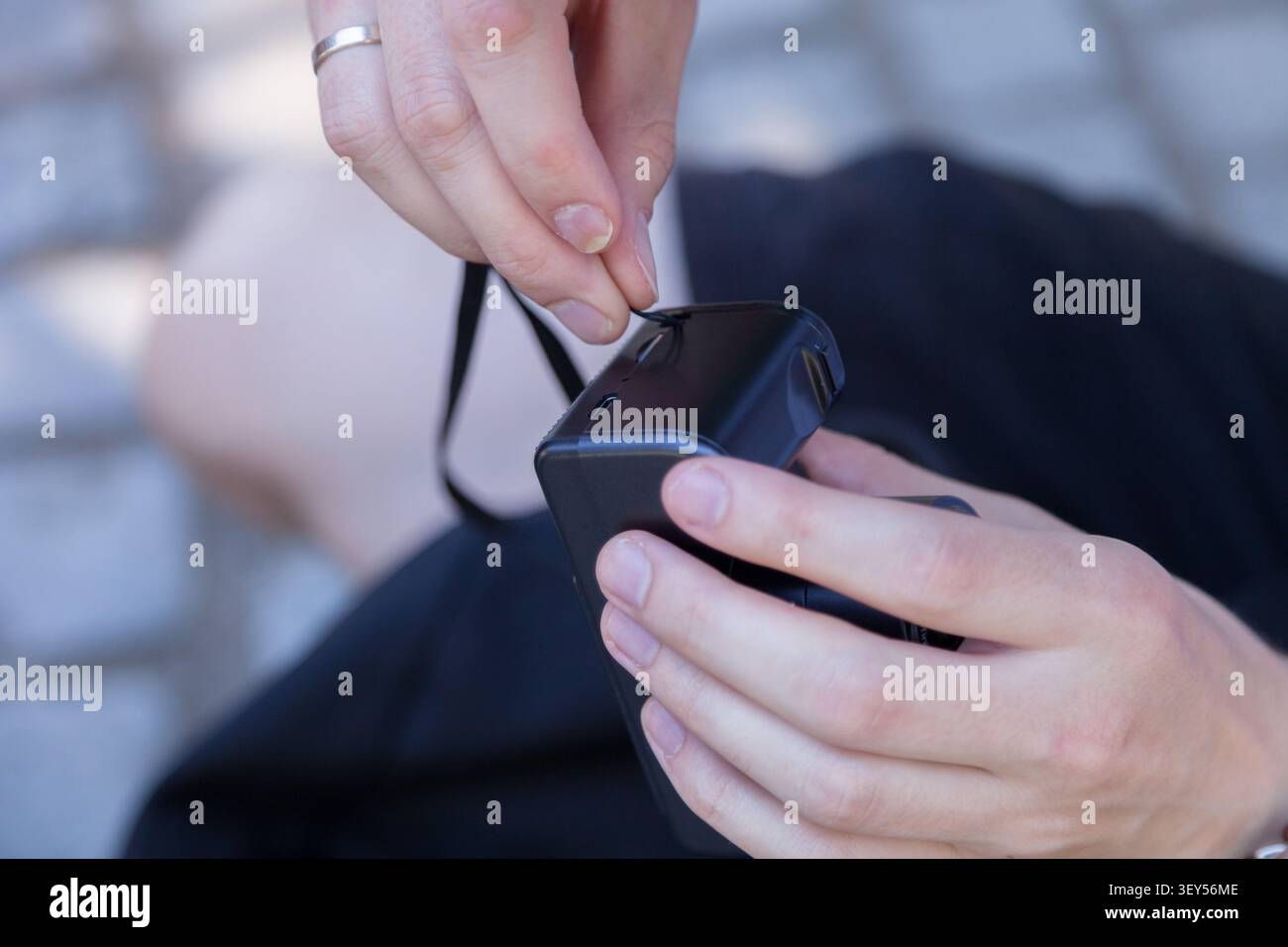 Mano che fissa il cinturino da polso alla fotocamera compatta. Preparazione della fotocamera e sicurezza delle attrezzature prima della fotografia Foto Stock