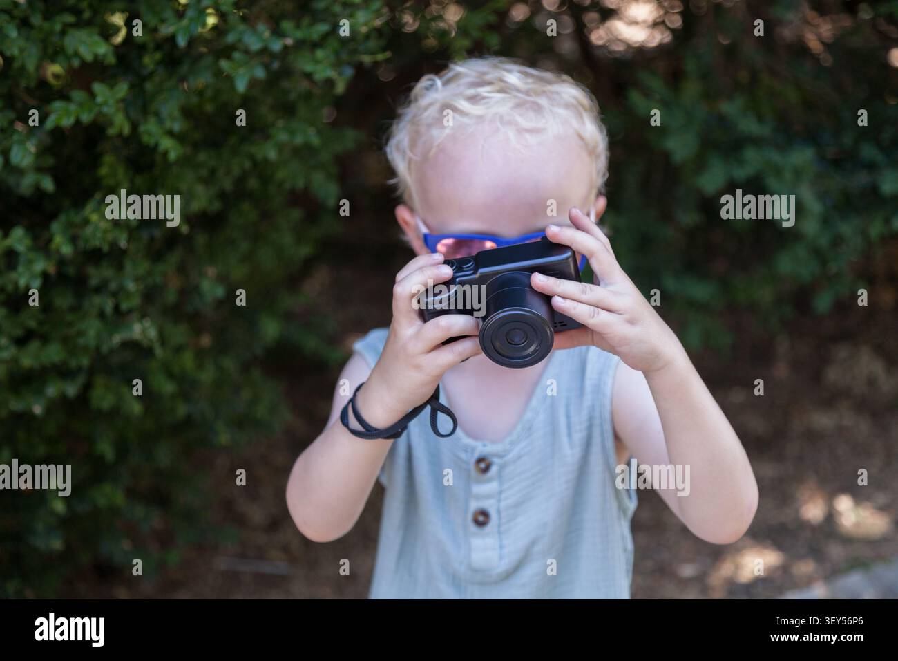 Bambino che tiene in mano una fotocamera compatta durante la composizione di una fotografia. L'interesse iniziale per la fotografia incoraggia la creatività Foto Stock