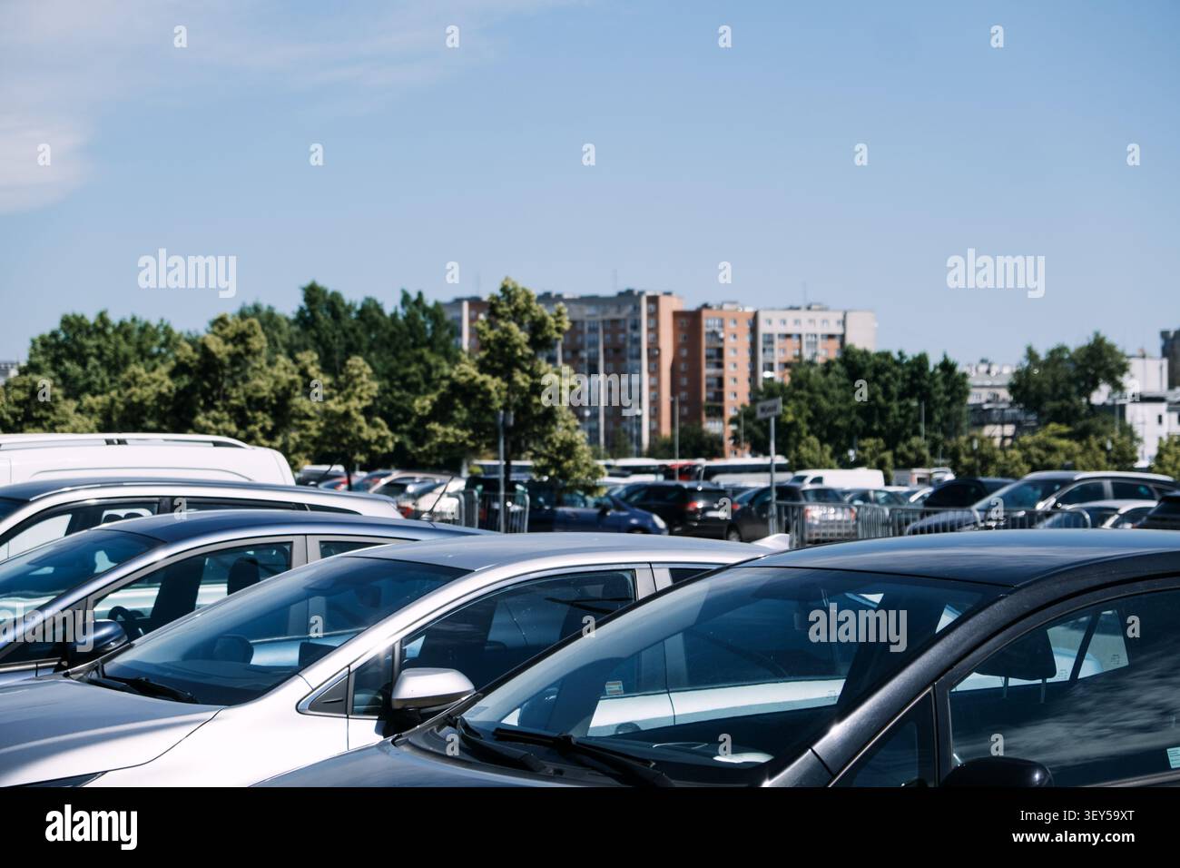 Una fila di auto parcheggiate riempie il terreno all'aperto di edifici residenziali e alberi verdi sotto il cielo azzurro. Parcheggio cittadino, parcheggio esterno affollato, urbano Foto Stock