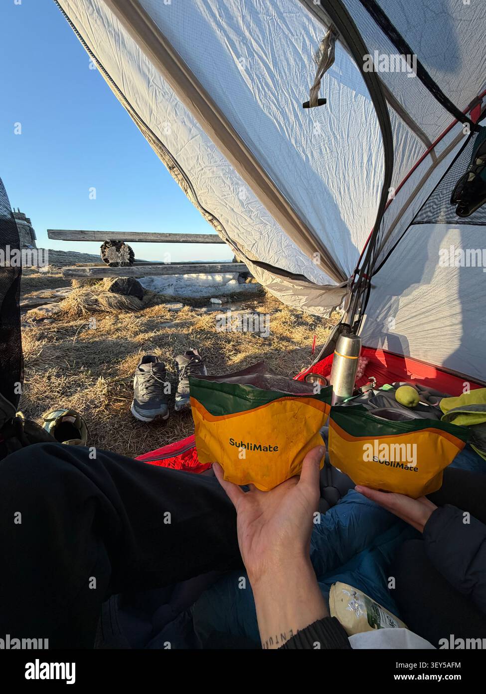Prospettiva in prima persona dall'interno della tenda che mostra i backpackers che tengono in mano buste di cibo da trekking liofilizzato presso il campeggio di montagna ad alta quota, con p Foto Stock