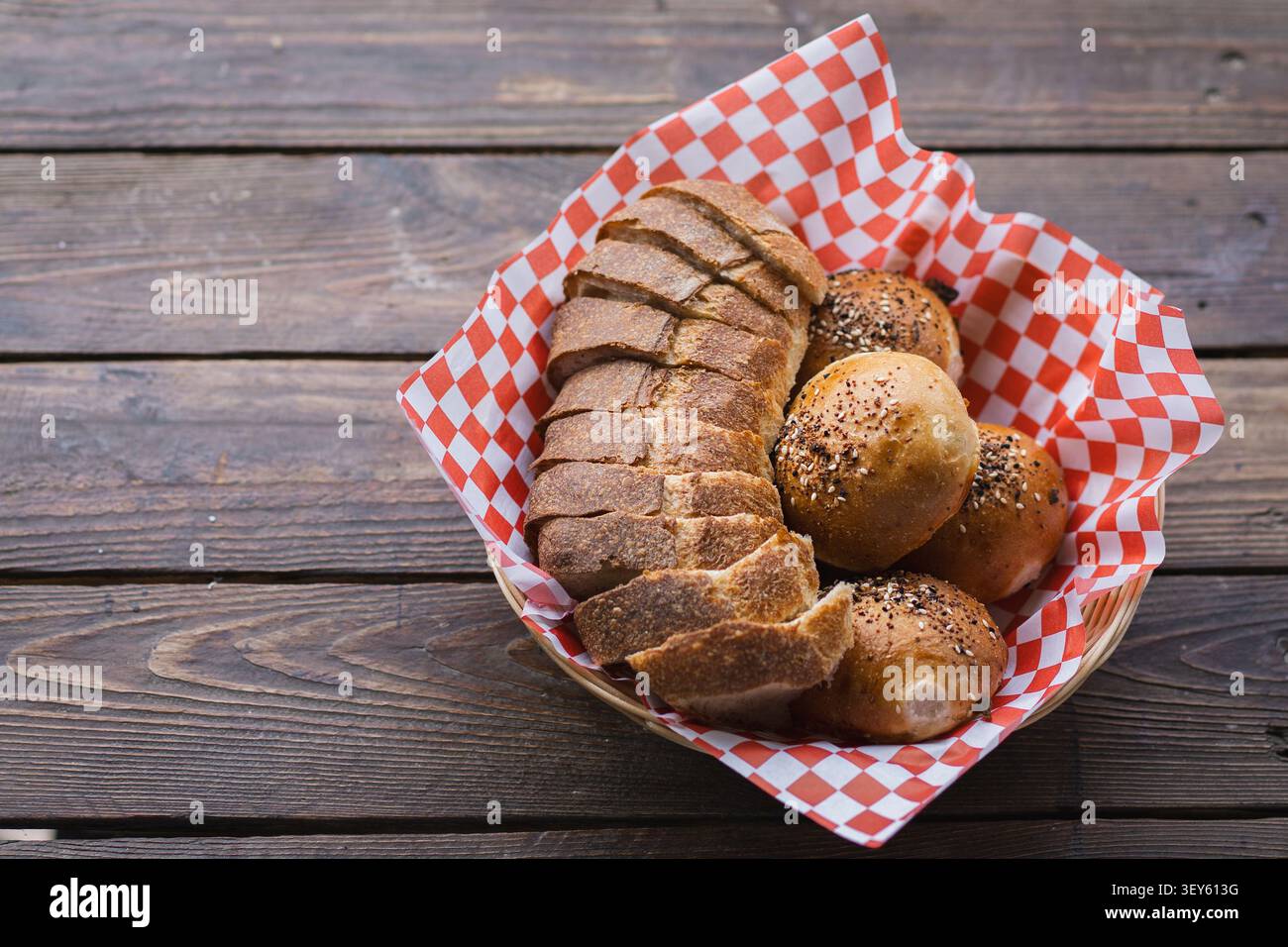 Pane artigianale con impasto di origine e rotoli di semi serviti nel cestino su tavolo di legno Foto Stock