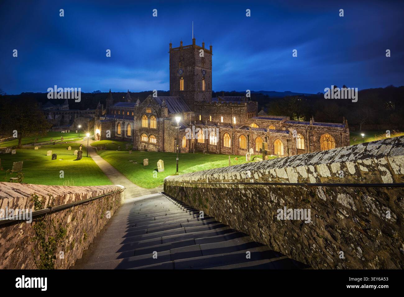 Cattedrale di St Davids a St Davids, Pembrokeshire, Galles, Regno Unito, illuminata al crepuscolo, vista dai gradini che portano al cimitero. Foto Stock