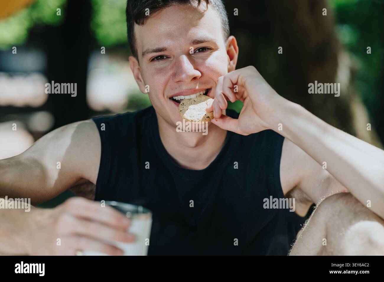 Un giovane che fa escursioni all'aperto sorseggiando un biscotto e un bicchiere di latte mentre sorride e riposa Foto Stock