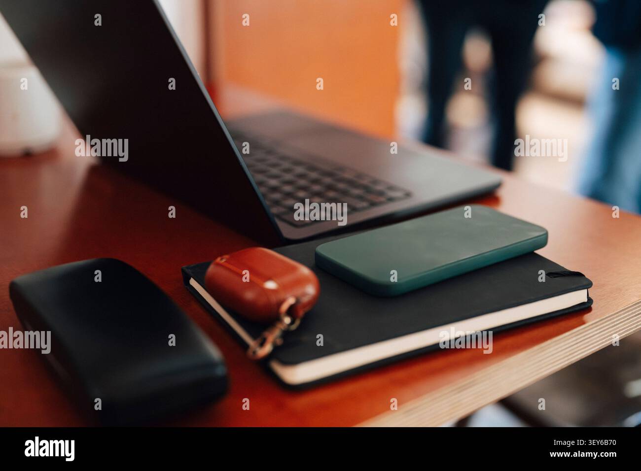 Primo piano di uno smartphone in una custodia verde appoggiato su un diario nero accanto al laptop in un moderno spazio di coworking Foto Stock