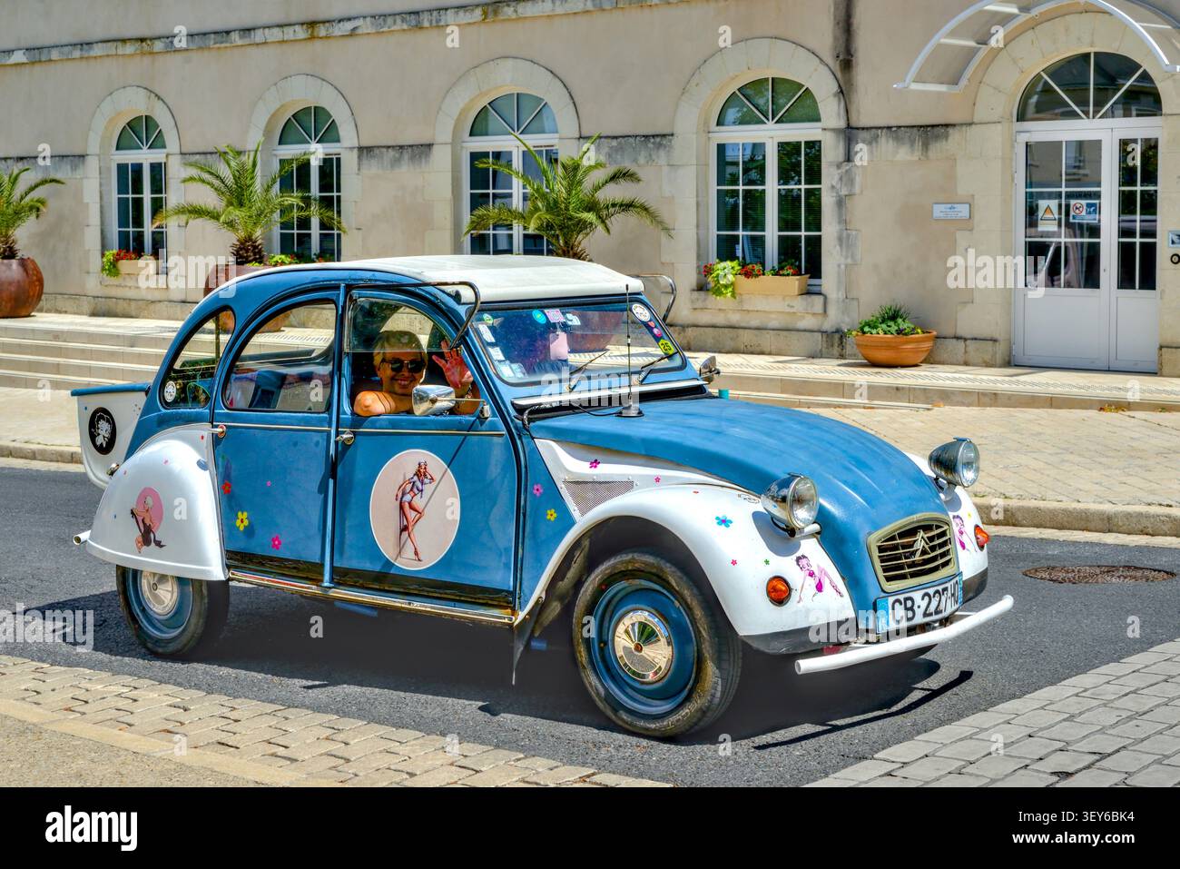 Donna che sventola dalla Citroen 2CV degli anni '1970 in Glacier Blue e White con "big boot" aggiunta alla parte posteriore della carrozzeria - la Roche Posay, Vienne (86), Francia. Foto Stock