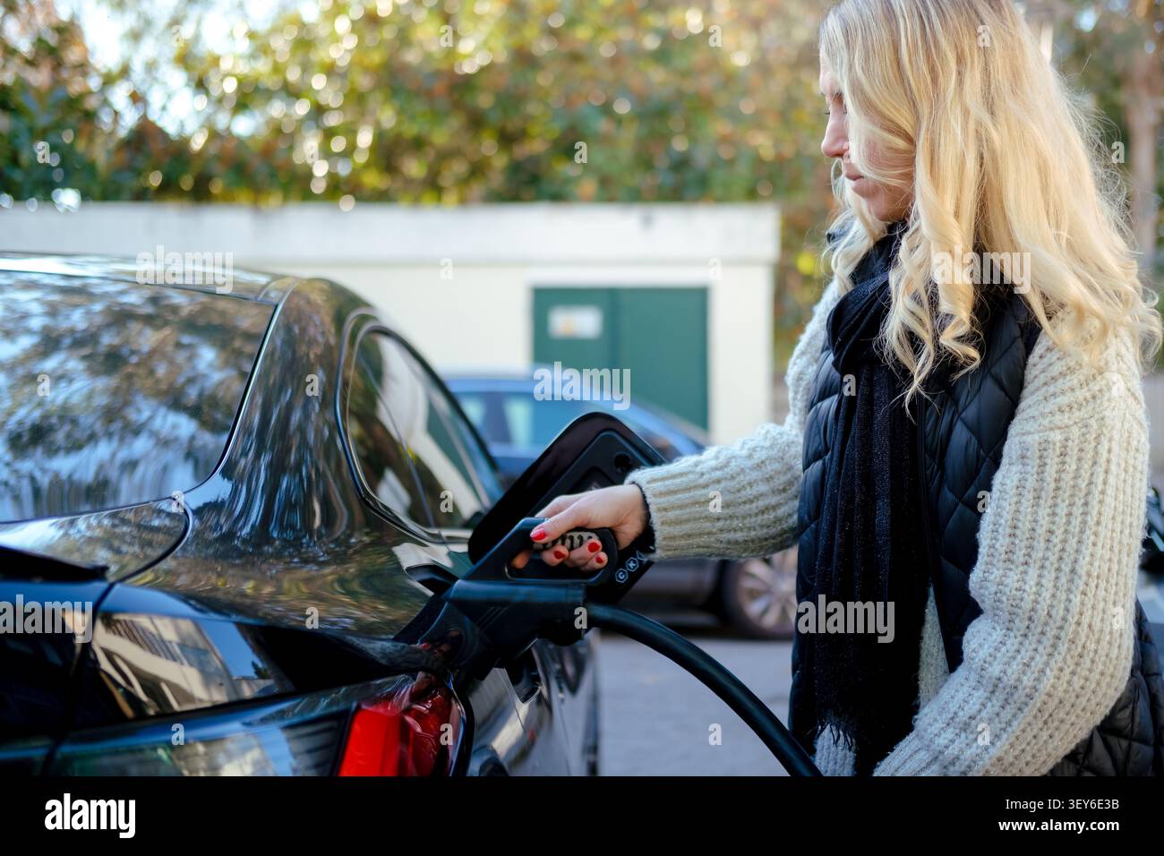 La mano della donna collega il cavo all'auto elettrica per ricaricare la sua batteria Foto Stock