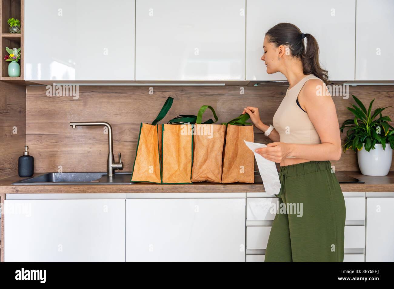 Donna che controlla la ricevuta della spesa e guarda all'interno di borse riutilizzabili dopo la consegna a domicilio. Verifica dell'ordine e concetto di controllo del consumatore Foto Stock