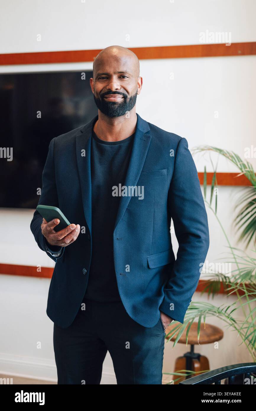 Ritratto di un uomo d'affari che tiene in mano il telefono mentre si trova in tasca sullo spazio di lavoro Foto Stock