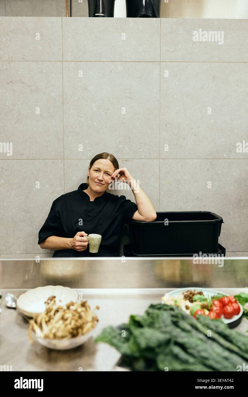 Chef donna appoggiata su una cassa mentre si siede nell'area di servizio durante la pausa Foto Stock