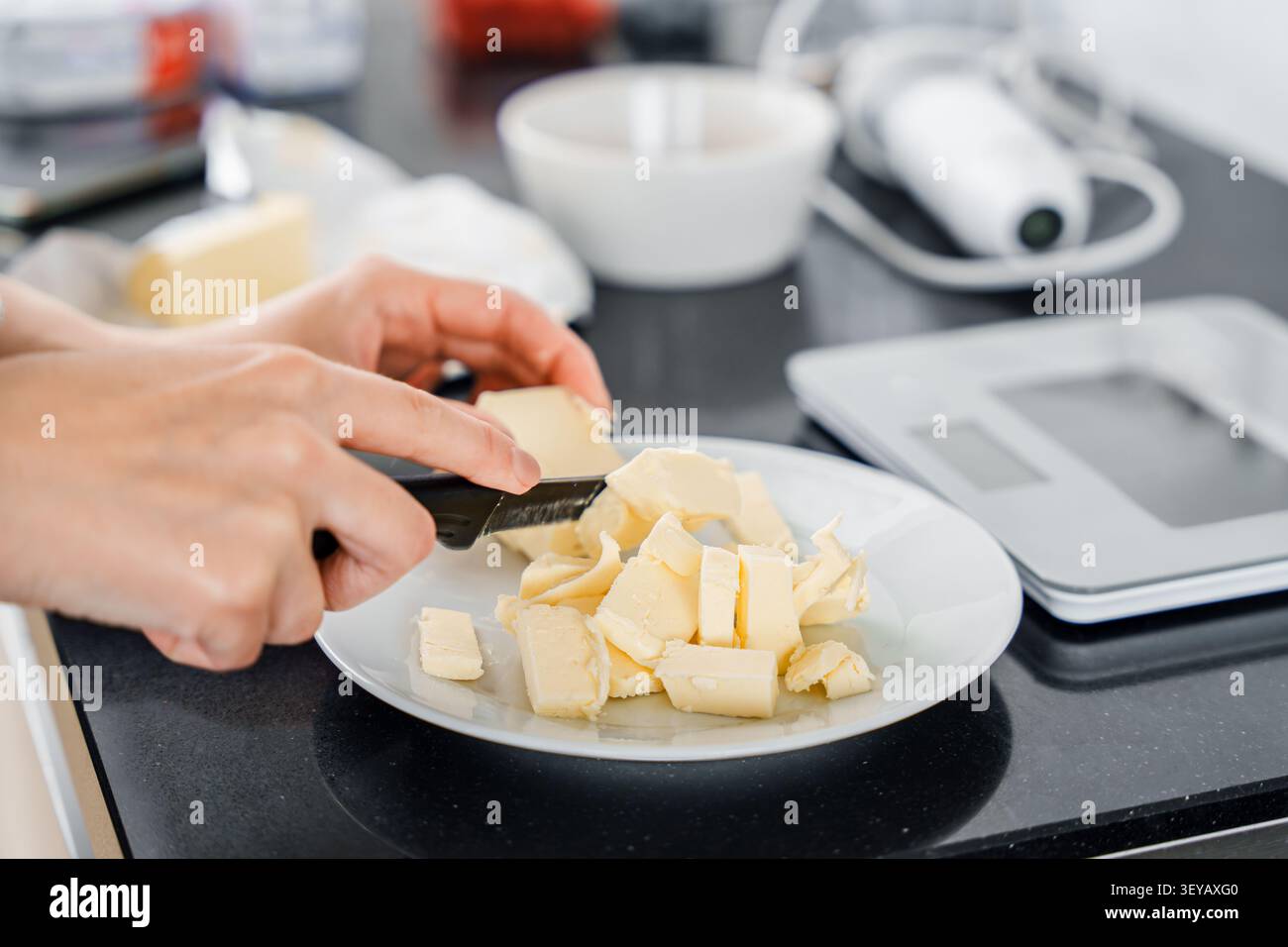 Le mani affettano il burro freddo in piccoli pezzi mentre preparano gli ingredienti per dolci fatti in casa, pasticceria o ricette di biscotti in cucina, preparazione della ricetta, Foto Stock