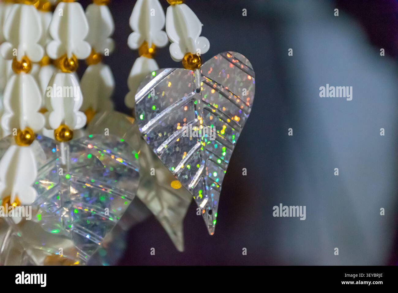 Primo piano di scintillanti ornamenti sospesi in foglia di cristallo con perle floreali bianche che riflettono una luce colorata, ideale per la decorazione, l'artigianato di lusso e. Foto Stock