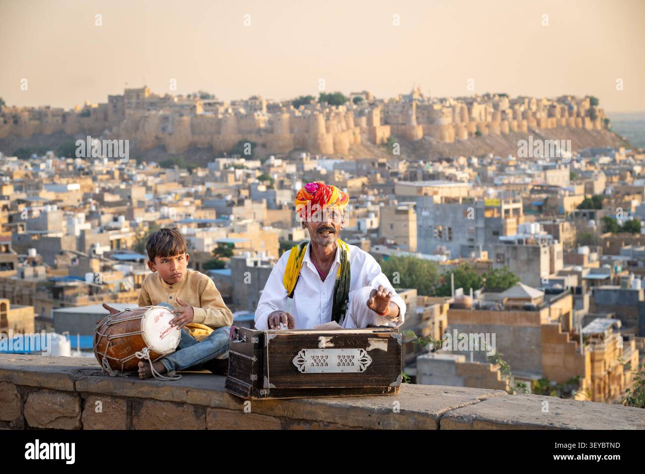 Musicisti di strada che suonano musica folk del Rajasthan su un armonio con il Forte di Jaisalmer sullo sfondo, Jaisalmer, Rajasthan, India Foto Stock