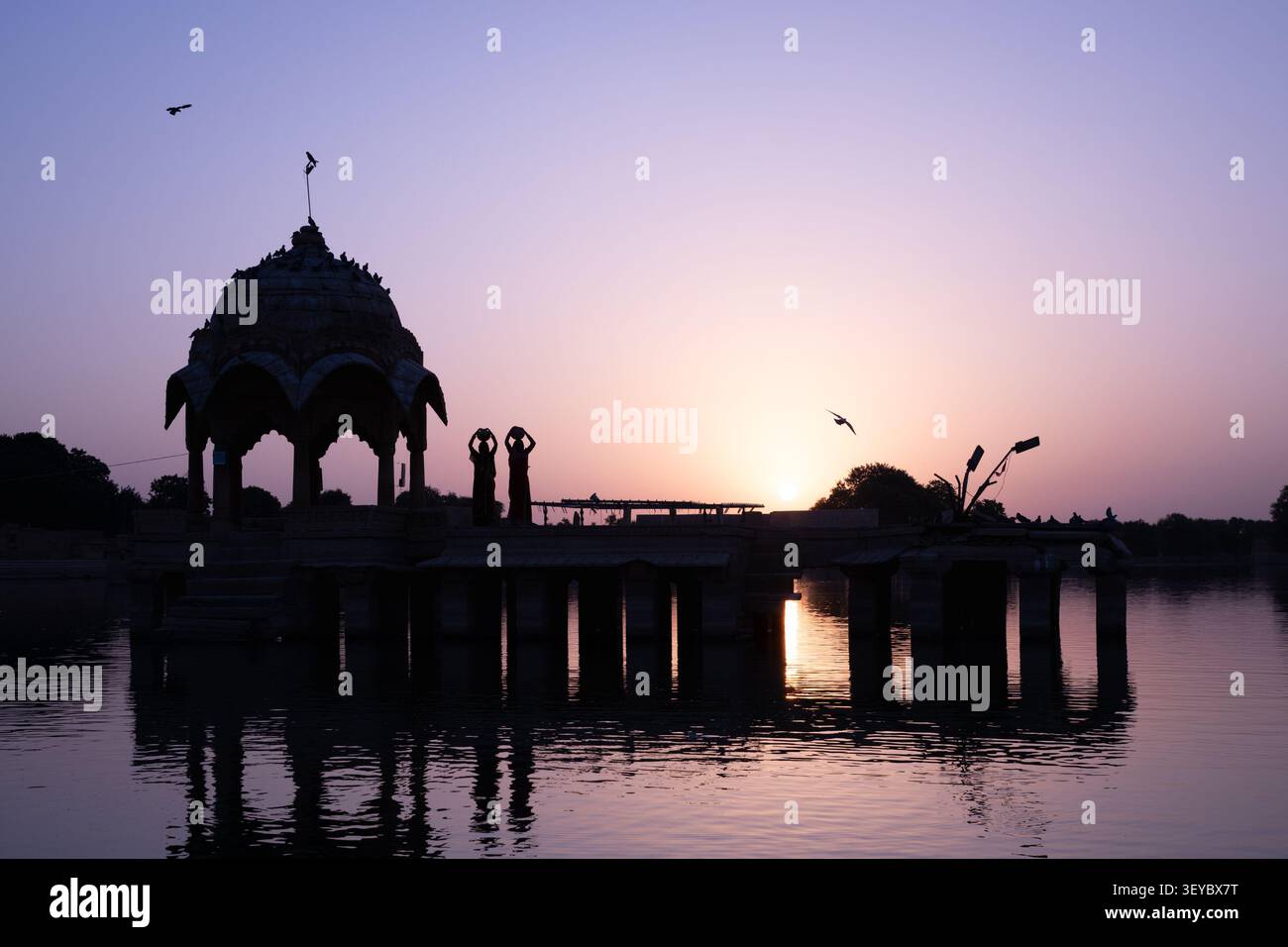 Due donne che portano brocche d'acqua su un padiglione a cupola al lago Gadisar all'alba a Jaisalmer, Rajasthan, India Foto Stock
