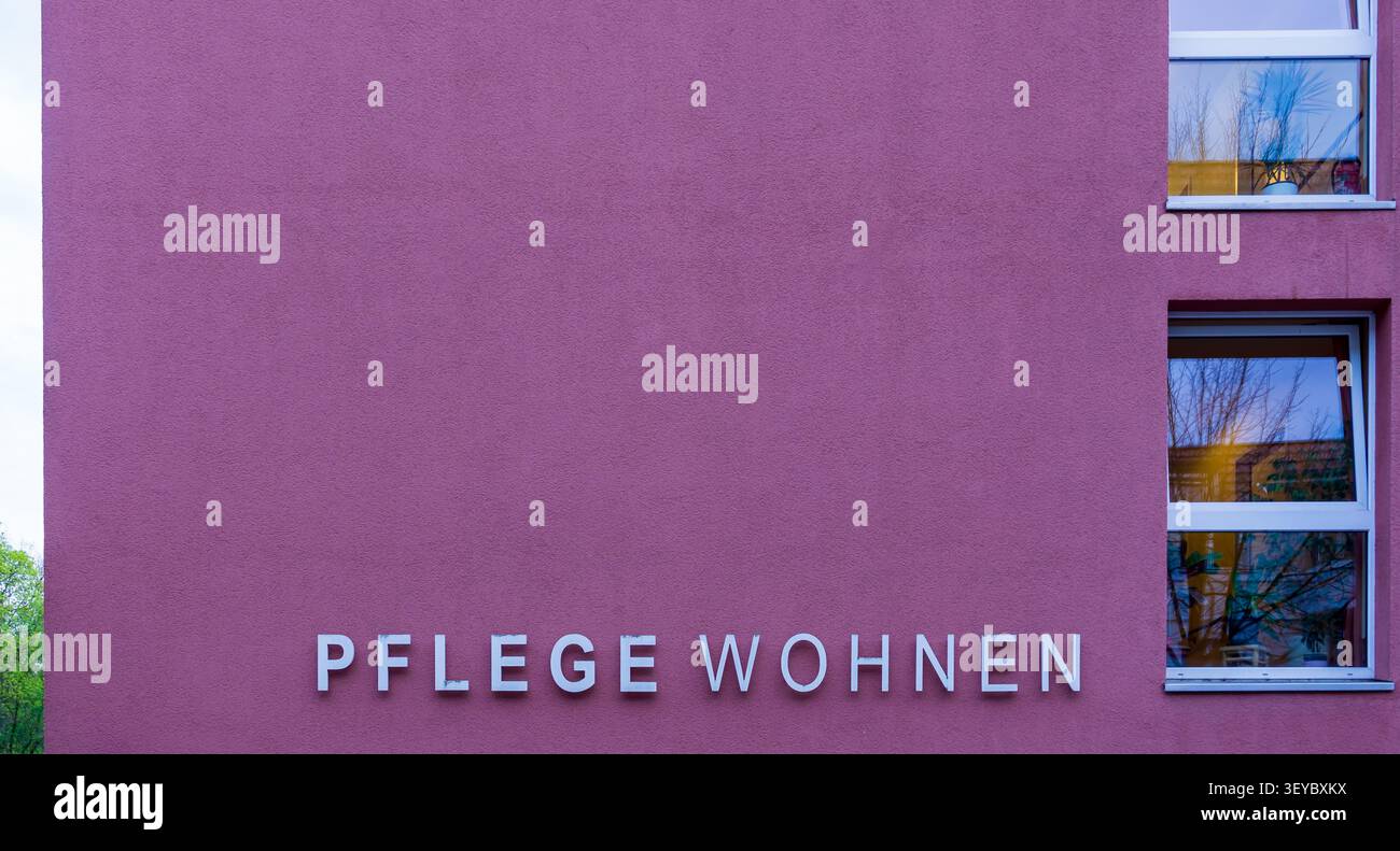 Primo piano di una moderna facciata di una casa di riposo con le parole tedesche "Pflege Wohnen" (abitazione assistita) su una parete esterna viola. Pflegeheim, Altersheim. Foto Stock