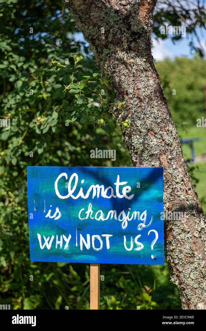 Segno del clima di base: “Il clima sta cambiando, perché non noi?” Immerso nel verde Foto Stock