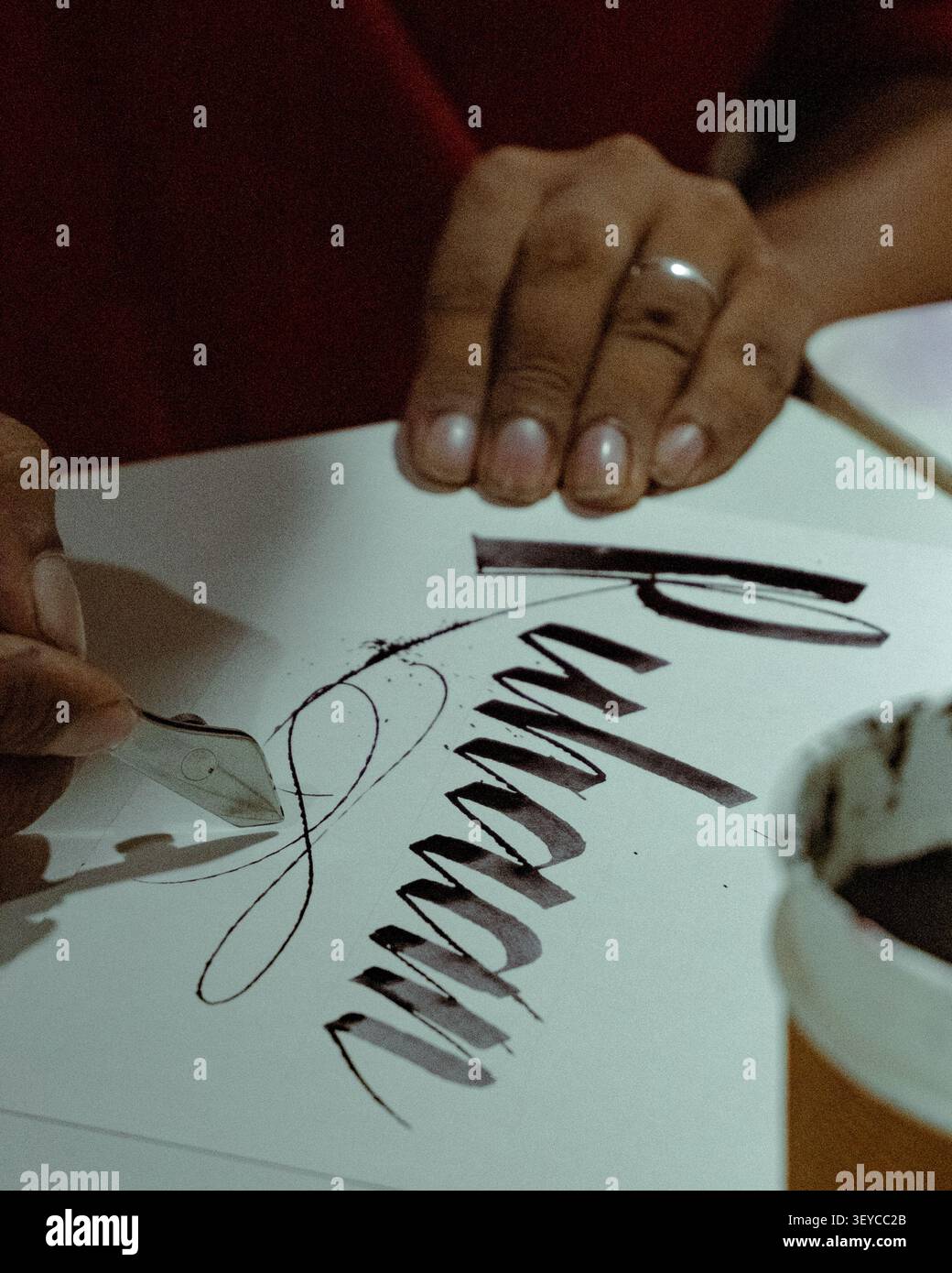 Primo piano di un calligrafo che crea una moderna scrittura a mano con una penna a immersione e inchiostro nero su carta bianca durante una sessione di pratica calligrafica. Foto Stock