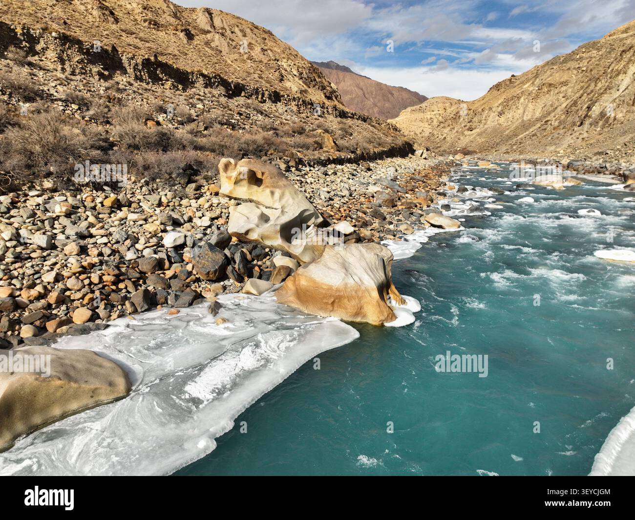 Colpo a livello di occhio di un fiume glaciale turchese con grandi massi scolpiti e calotte di ghiaccio bianche pressate contro la sponda rocciosa e arida del fiume Foto Stock