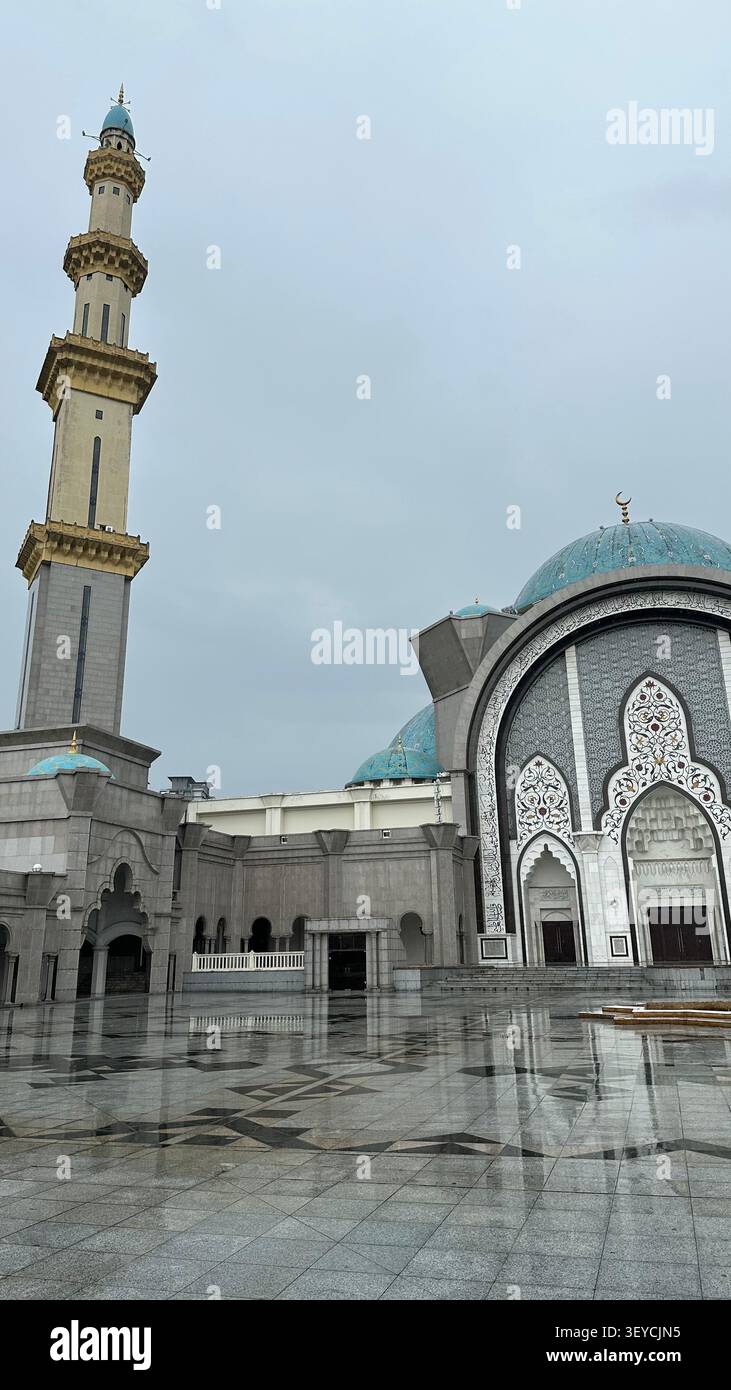 Grande cortile della moschea del territorio federale di Kuala Lumpur, Malesia, con minareto, cupola blu ornata e intricato arco islamico riflesso sulla marba bagnata - Immagine stock catturata con smartphone