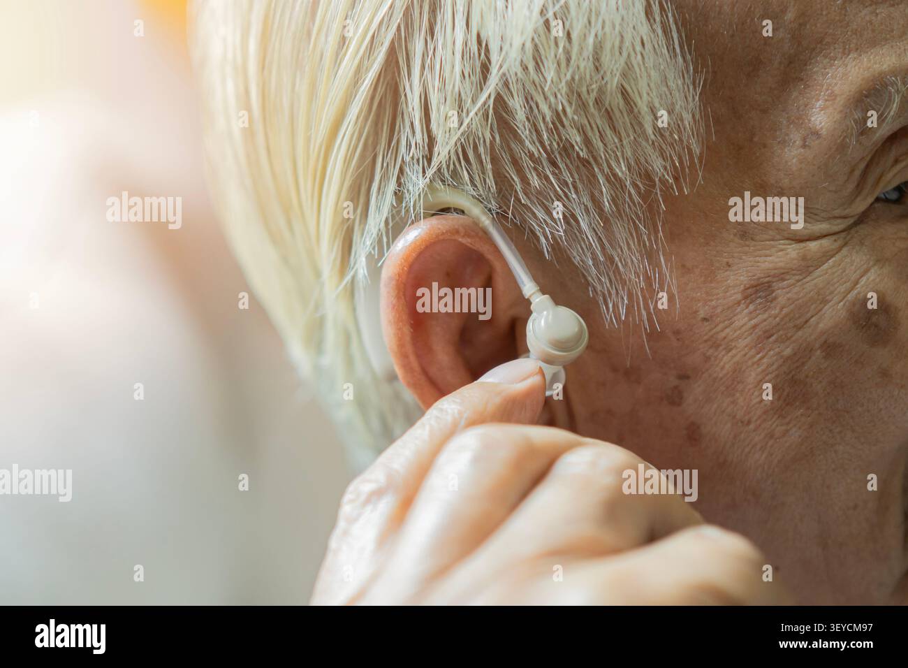 Primo piano di un anziano dai capelli grigi che usa il suo apparecchio acustico nell'orecchio con spazio di copia. Concetto di perdita dell'udito e problemi all'orecchio. Foto Stock