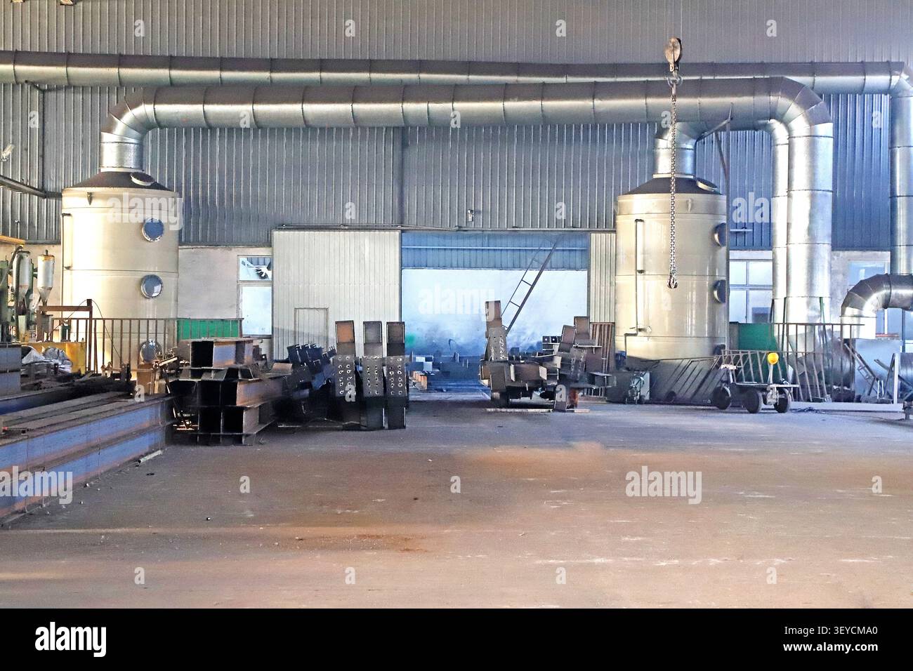 Un'immagine ampia e grandangolare dell'interno di una fabbrica industriale pesante, con due grandi torri cilindriche di controllo dell'inquinamento atmosferico e un gancio per carroponte Foto Stock