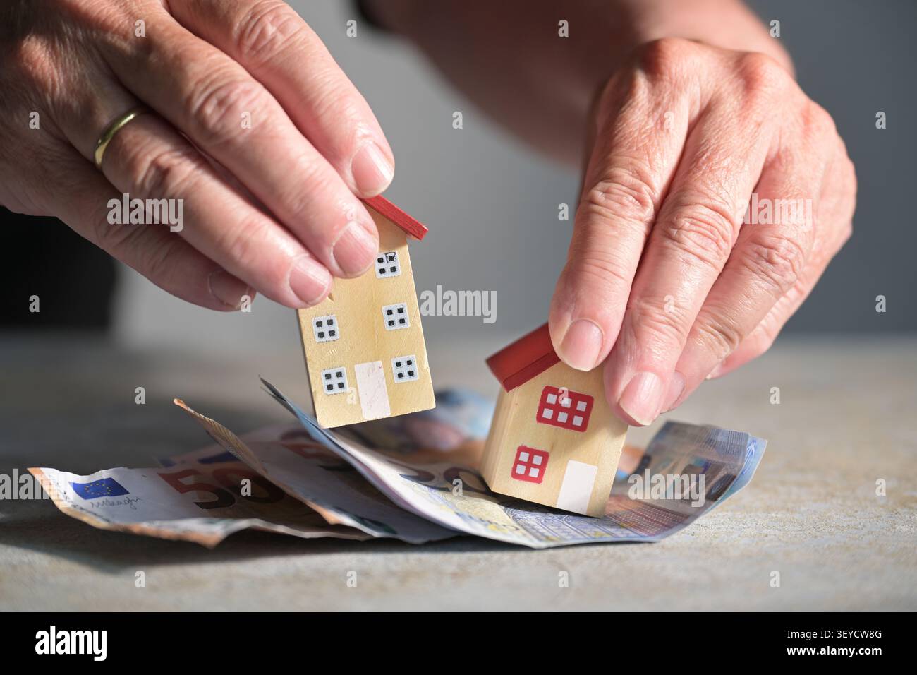 Mani anziane che mettono una grande e una piccola casa in miniatura sulle banconote, decidono se investire in immobili commerciali o in una casa di famiglia, sele Foto Stock