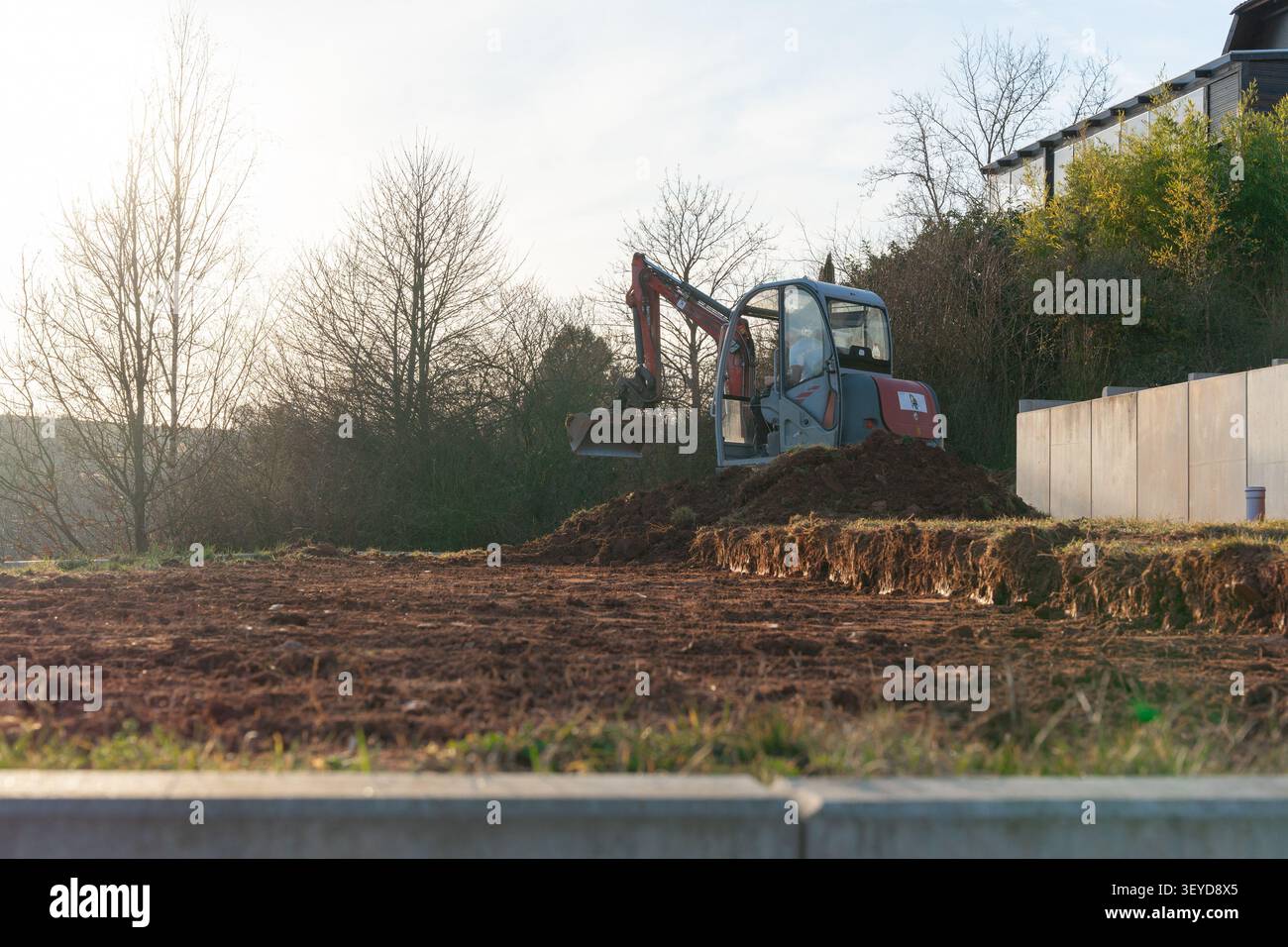 L'escavatore, dotato di una benna, rastrella terreno argilloso mescolato a pietre. I macchinari pesanti stanno lavorando diligentemente nel cantiere Foto Stock